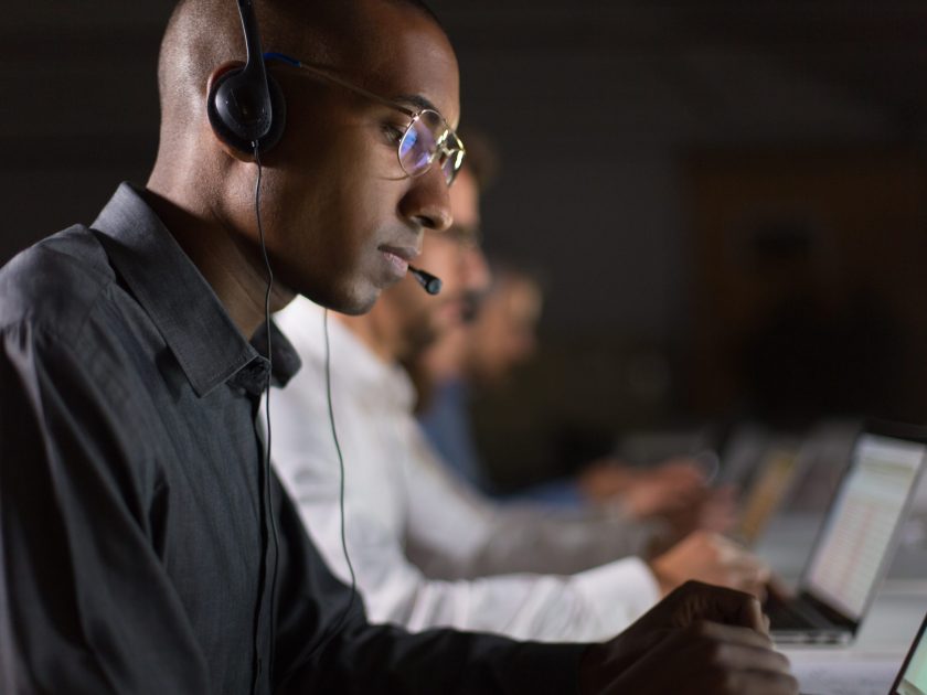 Focused call center operator typing on laptop. African American young man in eyeglasses looking at laptop at workplace. Call center concept